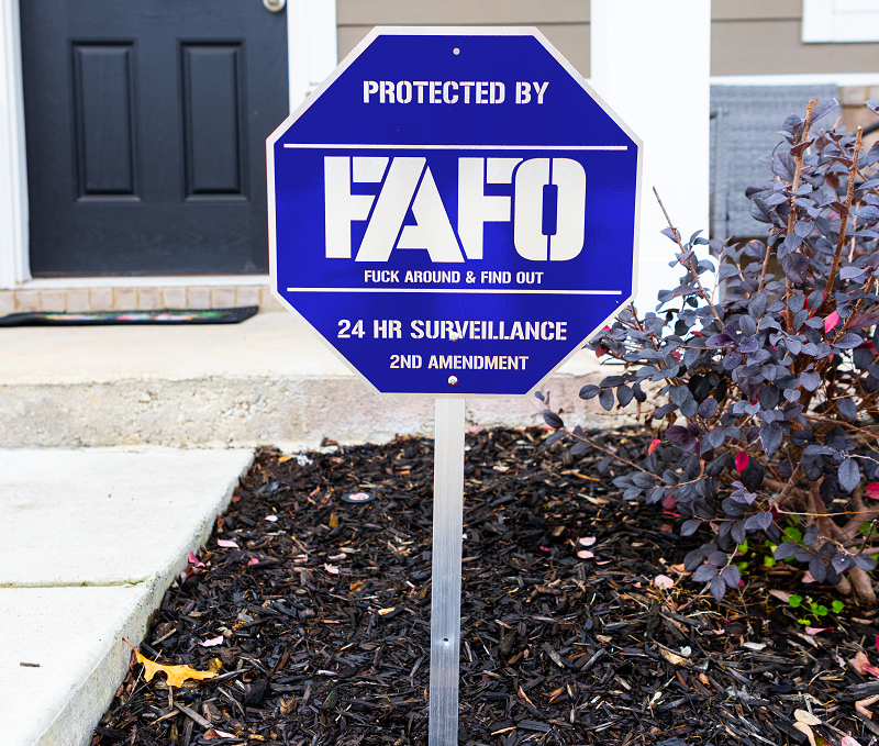 Protected By FAFO metal sign with 24 HR surveillance and 2nd Amendment, displayed in a garden setting.